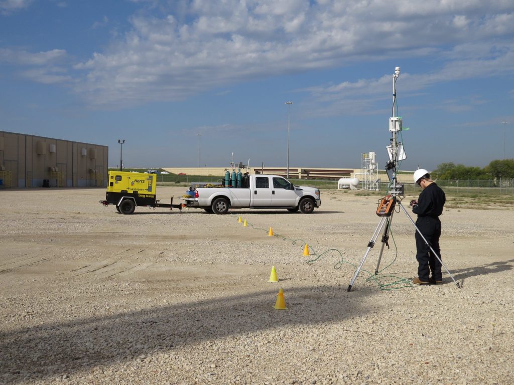 Worker setting up methane measurement equipment in a field location.